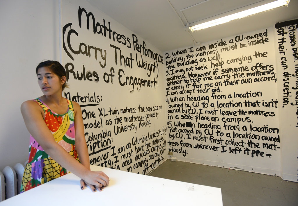 Η Emma Sulkowicz στο στούντιο τέχνης της. Στους τοίχους γραμμένοι οι κανόνες της εργασίας της “Carry That Weight”, μια διαμαρτυρία ενάντια στον τρόπο αντιμετώπισης κατηγοριών σεξουαλικής επίθεσης στην Πανεπιστημιούπολη από τον ίδιο το Πανεπιστήμιο.